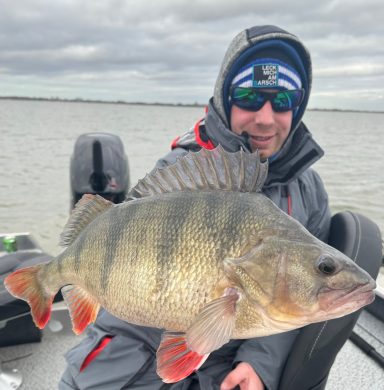Angler mit einem großen Zander, auf einem Boot, Hintergrund mit Wasser und Wolken.